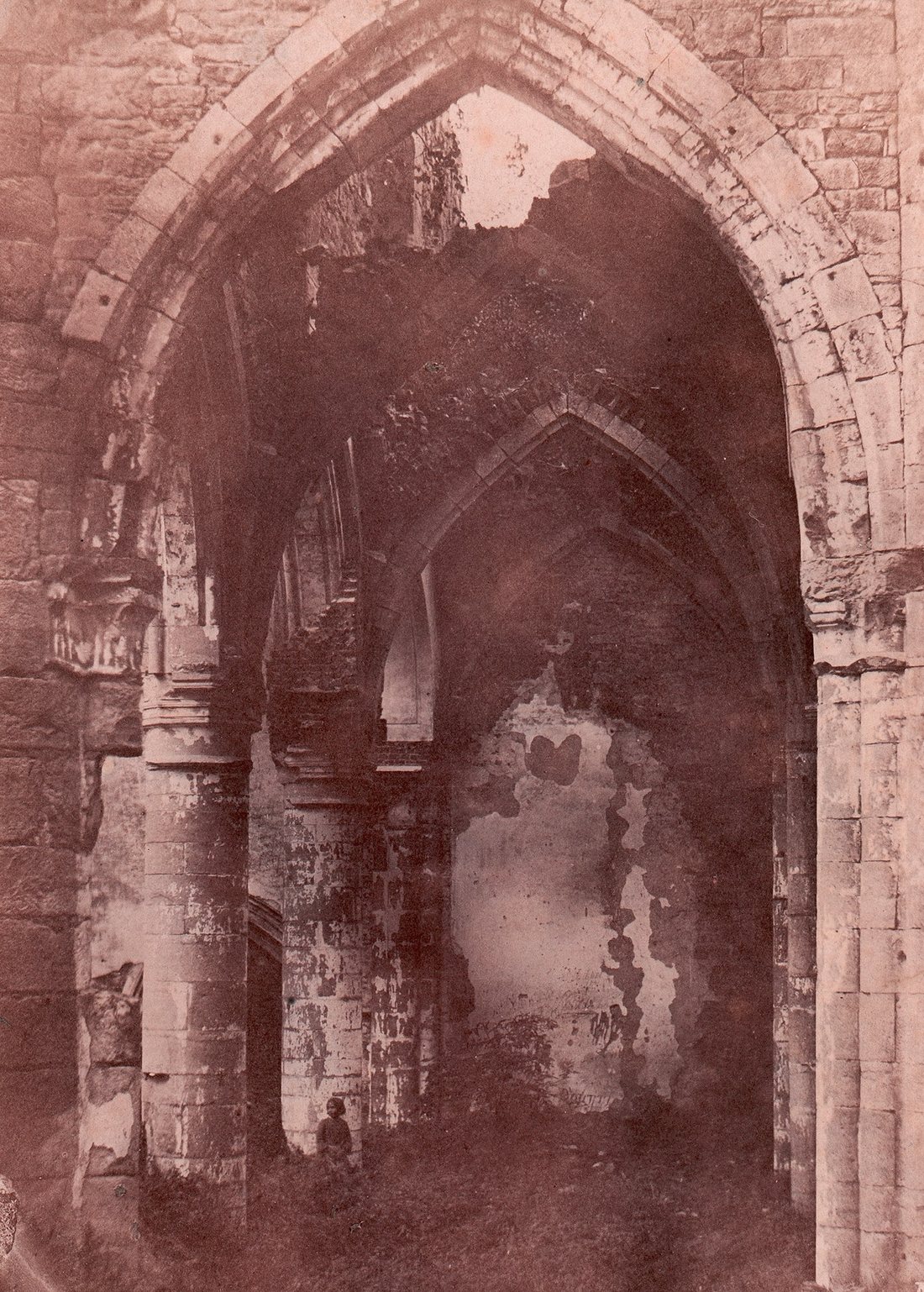 Nineteenth-century photograph of a ruined Gothic chapel interior, a small figure standing among the pillars